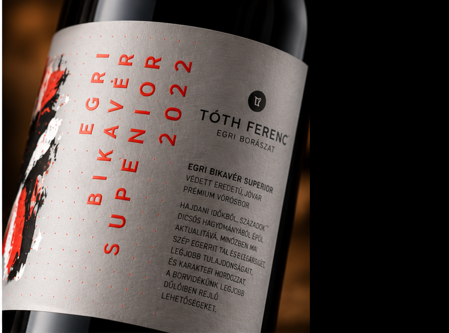 Close-up of a wine bottle label reading 'EGRI BIKAVÉR SUPERIOR 2022' and 'TÓTH FERENC', with a dark bottle background and red, black, and white label design.
