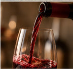 Red wine being poured from a bottle into a clear wine glass, with a warm blurred background.