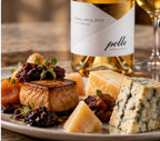 A plated food and wine spread featuring a bottle of Pelle Tokaji Aszu 2019 6 Puttonyos, alongside cheeses, cured meats, and fruit on a marble surface.