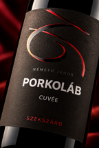 Close-up of a wine bottle label reading 'NÉMETH JÁNOS PORKOLÁB CUVÉE' with a dark textured background and red and gold abstract graphic accents.